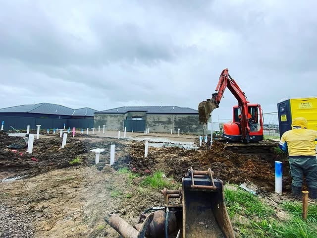 Mini excavator digging service trenches on a new estate block, worker watching