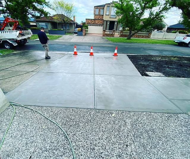 New exposed aggregate driveway with a plain concrete apron, worker hosing it down