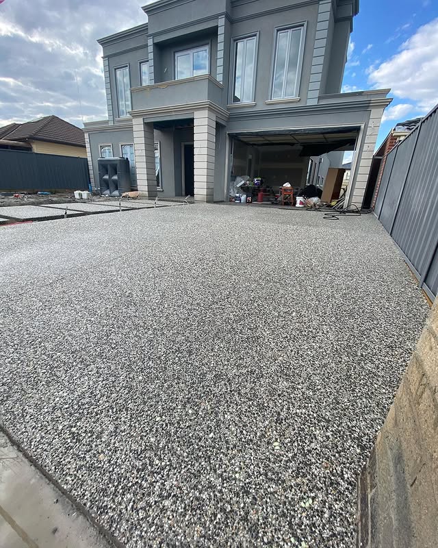 Wide exposed aggregate driveway leading up to a new grey two-storey home