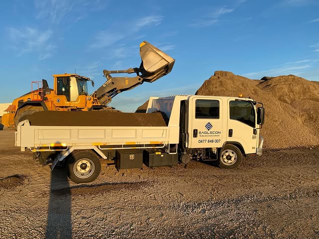 Front loader tipping soil into a tipper truck at a supply yard