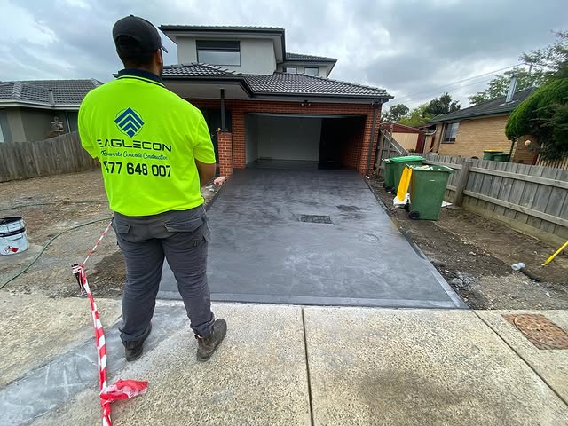 Worker in a hi-vis shirt beside a new charcoal concrete driveway