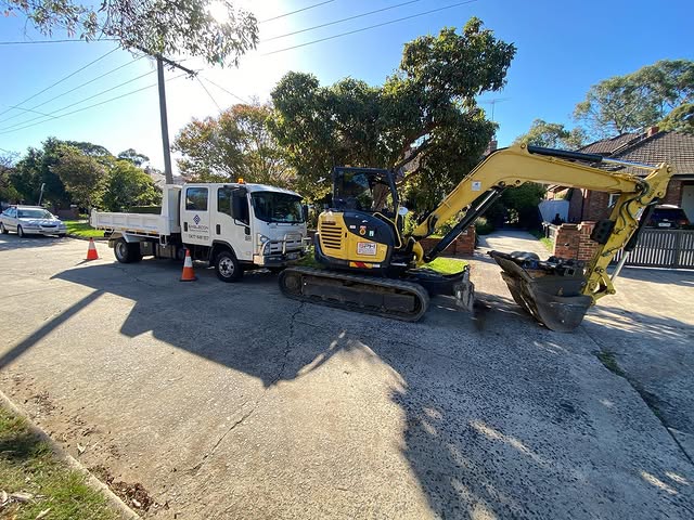 Excavator and tipper truck on a concrete driveway in a residential street
