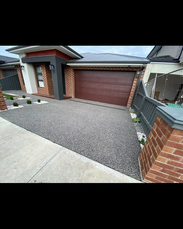 Exposed aggregate driveway leading to a brick home's timber garage door