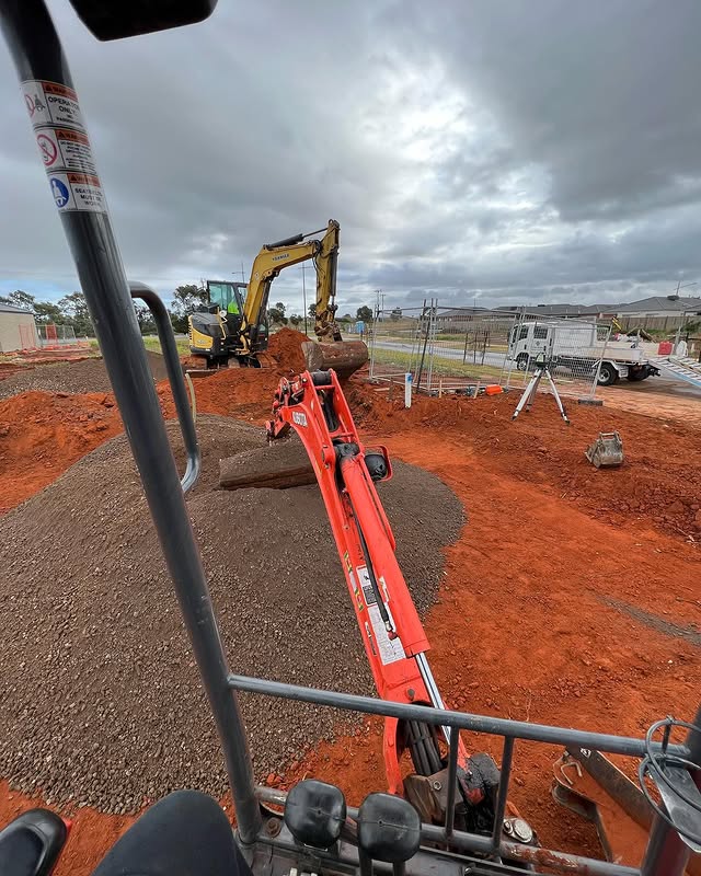 Mini excavator spreading crushed rock on a building site, seen from the cab