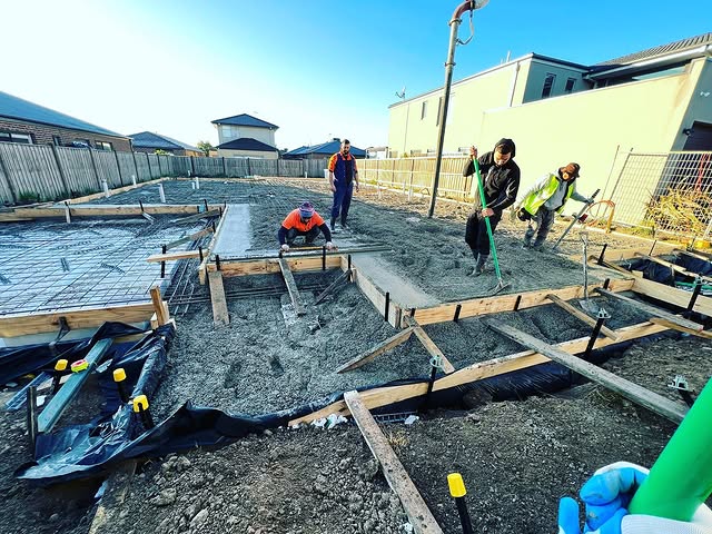 Crew raking crushed rock inside slab formwork before a pour
