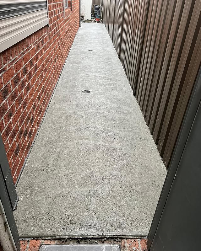 New concrete side path with a swirl finish between a brick wall and a fence