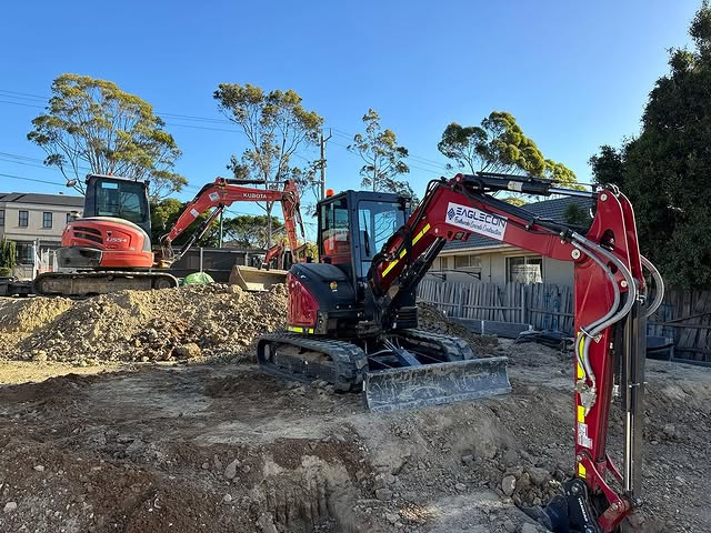 Two excavators on a cleared residential block beside mounds of soil
