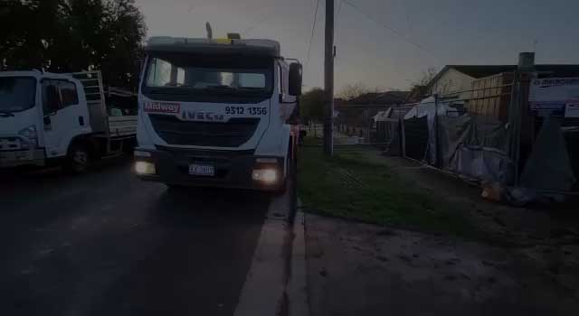 Truck with its headlights on beside a fenced building site at dusk