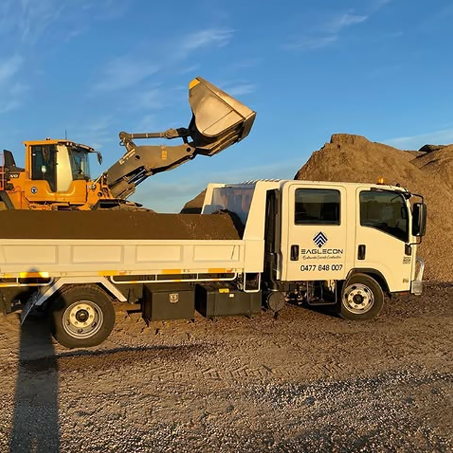Front loader tipping soil into a tipper truck at a supply yard