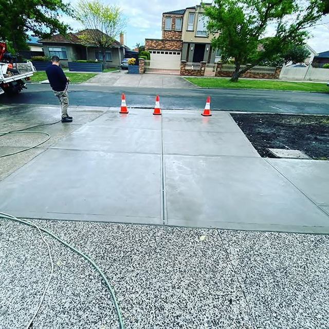 New exposed aggregate driveway with a plain concrete apron being hosed down