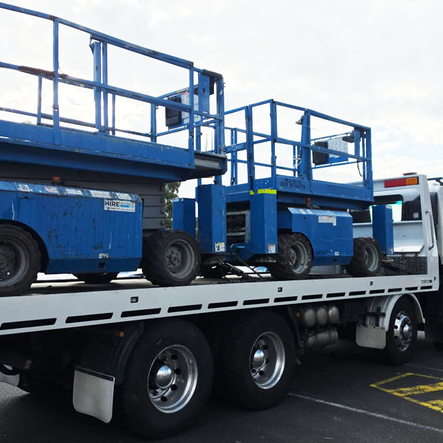 Truck carrying two blue scissor lifts on its tray