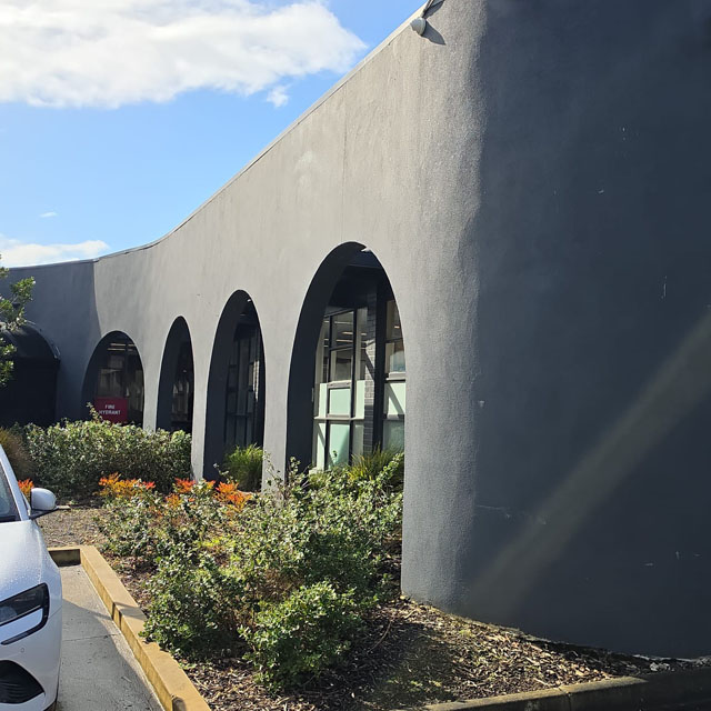 Dark grey building with arched windows and a landscaped garden bed