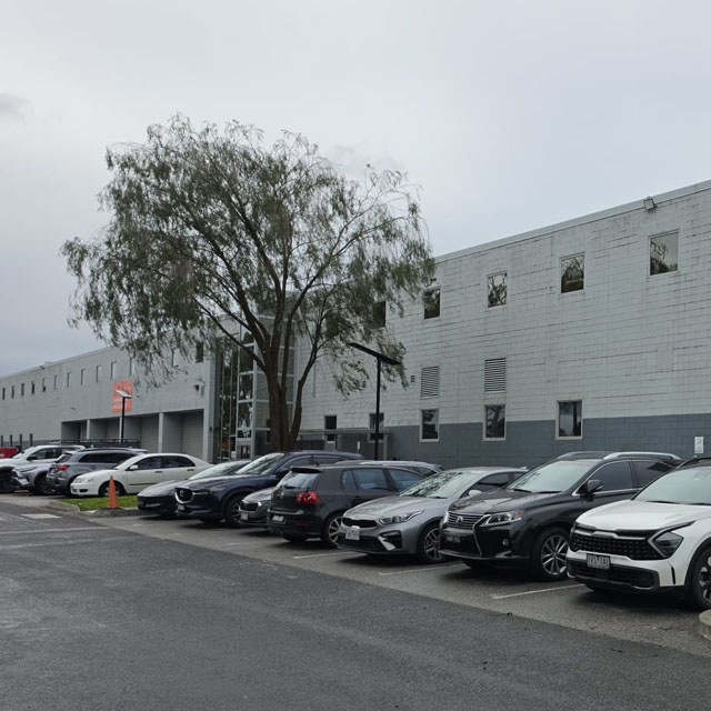 Rows of parked cars outside a long two-storey commercial building
