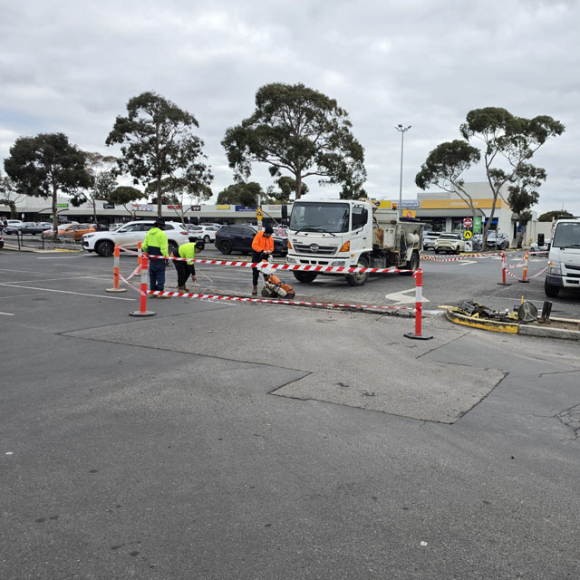 Car park works area closed off with cones and barrier tape, crew and truck nearby