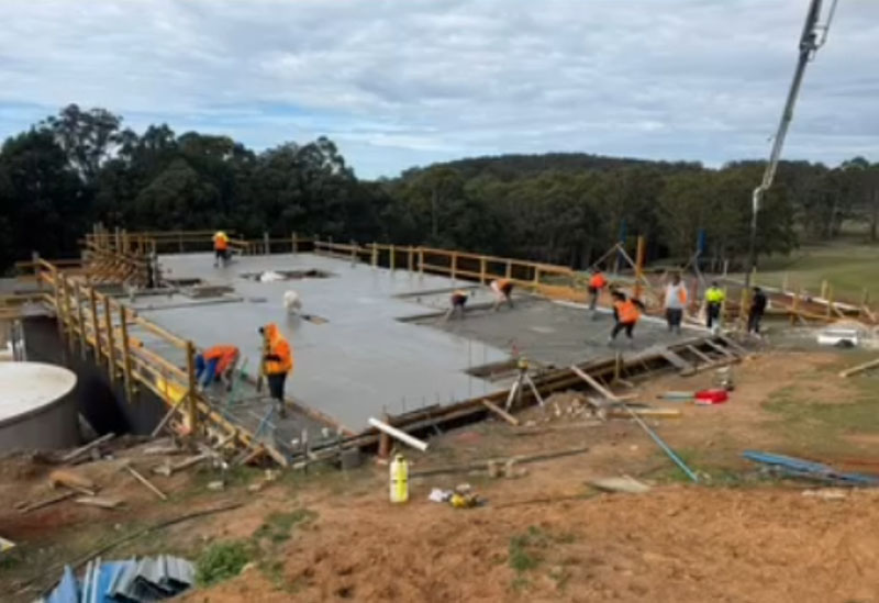 Crew placing a large concrete slab in timber formwork with a pump boom overhead