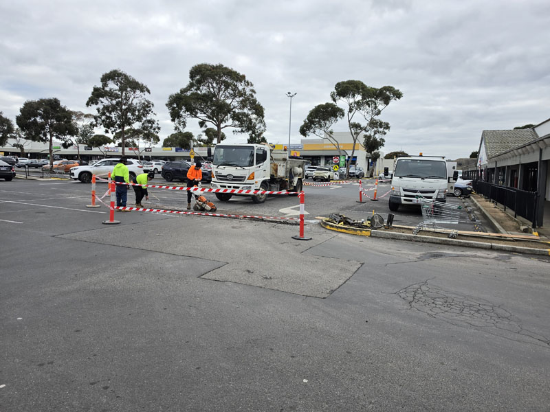 Car park works fenced off with cones and barrier tape, trucks and crew nearby