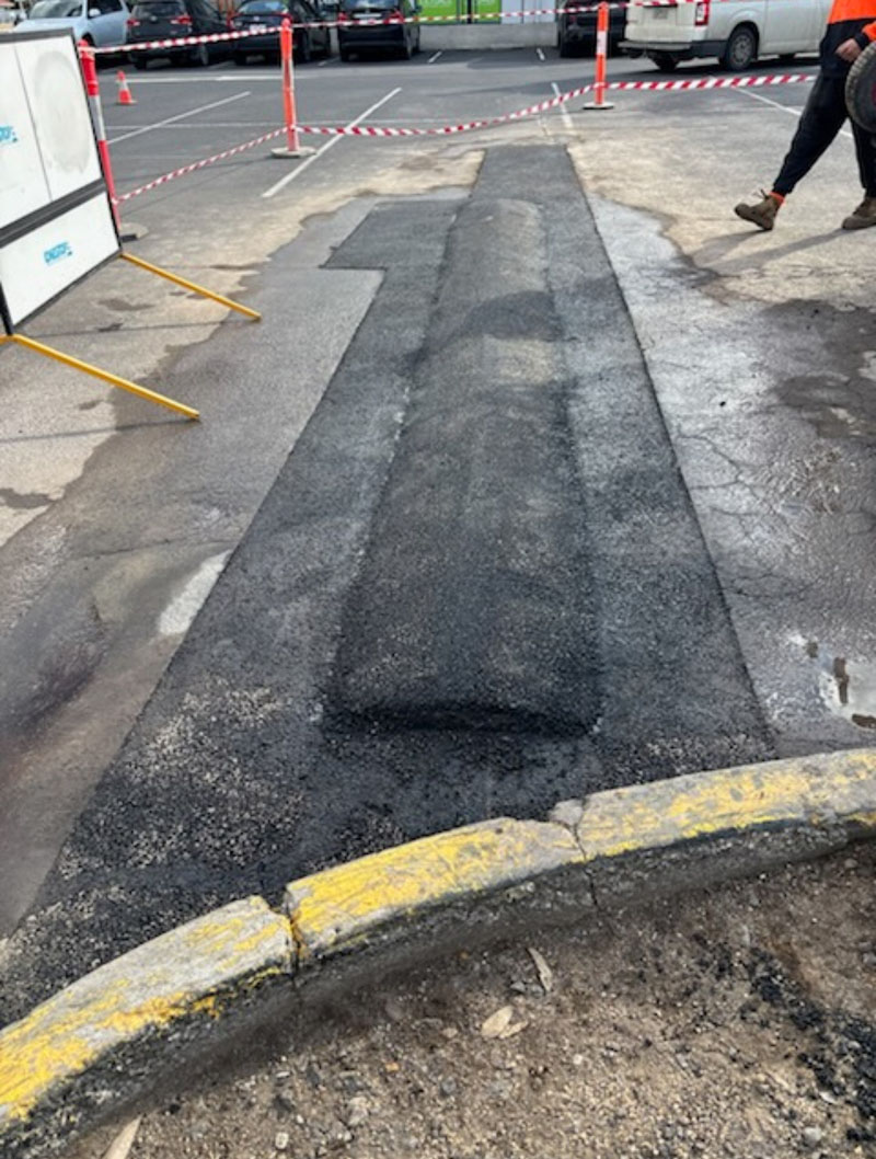 New asphalt strip laid across a car park beside a yellow kerb