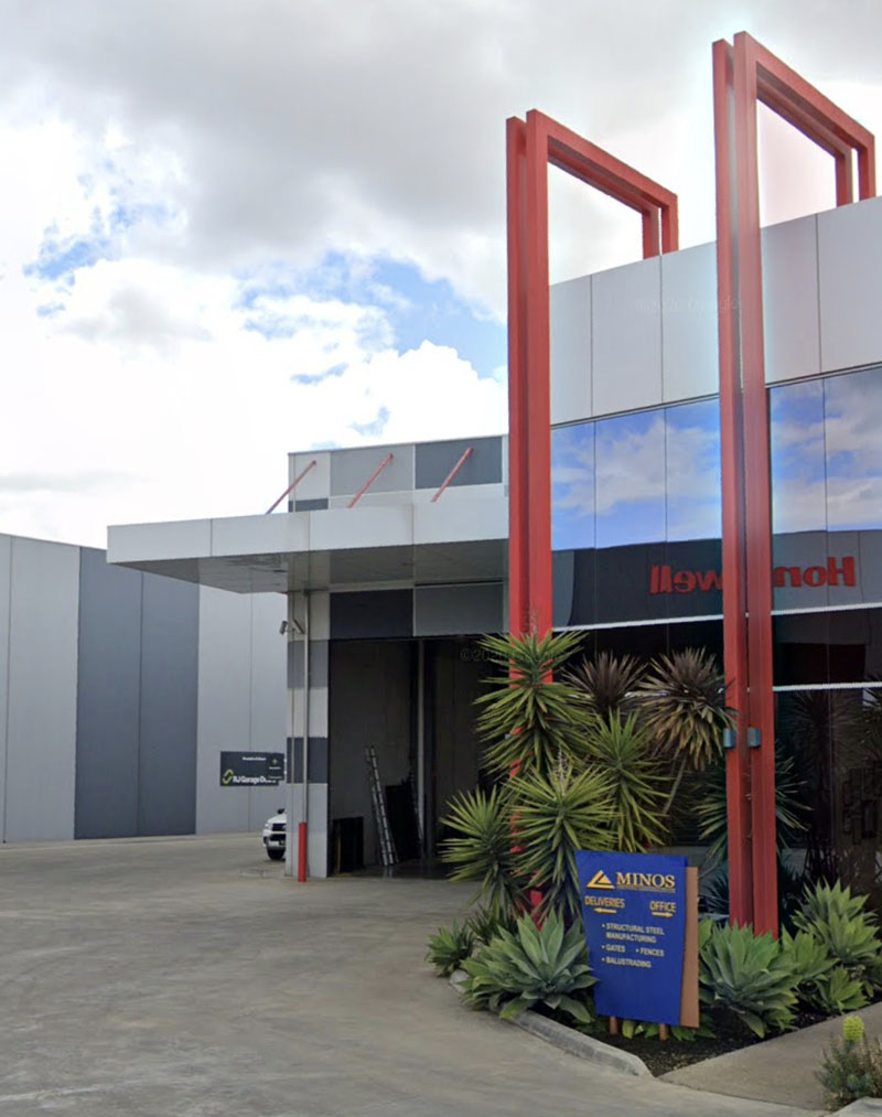 Office entrance with a tall red steel frame, palms and a garden bed