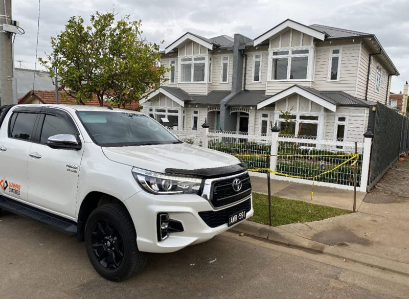 White ute parked outside a two-storey weatherboard home with a picket fence