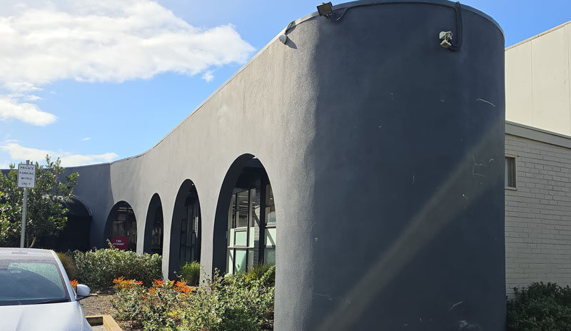 Grey rendered building with arched windows above a garden bed