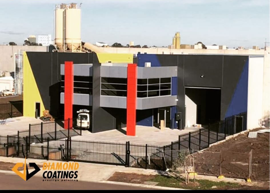 New industrial building with a black, red and yellow facade behind a black fence