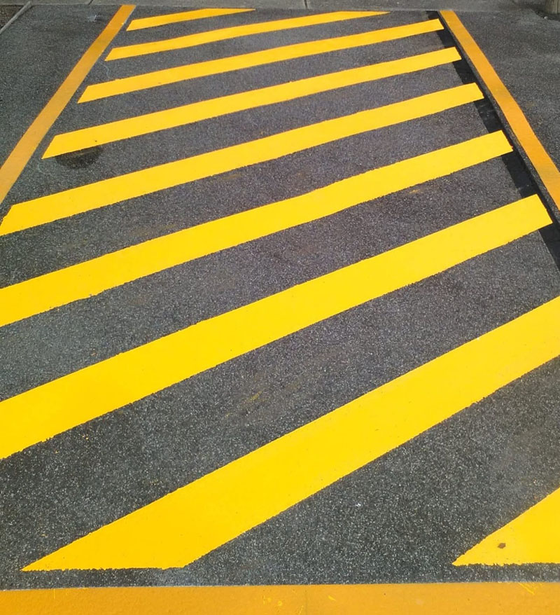 Fresh yellow hatched line marking on dark asphalt
