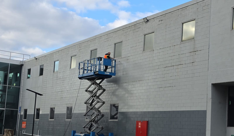 Worker on a scissor lift beside the wall of a grey block building