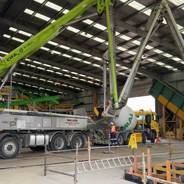 Concrete pump boom reaching into a large shed beside a concrete mixer truck