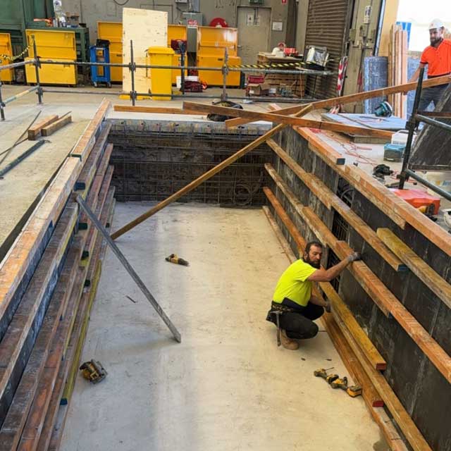 Worker in hi-vis inside timber formwork for a deep concrete pit in a factory
