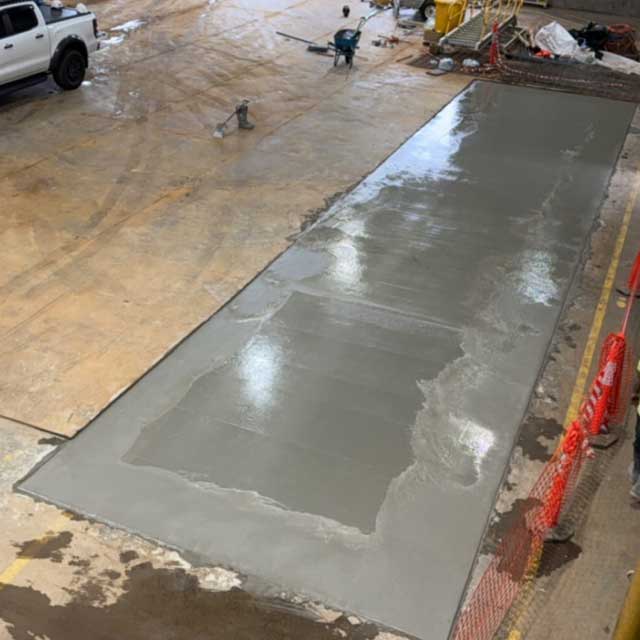 Freshly poured concrete strip in a warehouse floor, fenced off with orange barrier mesh