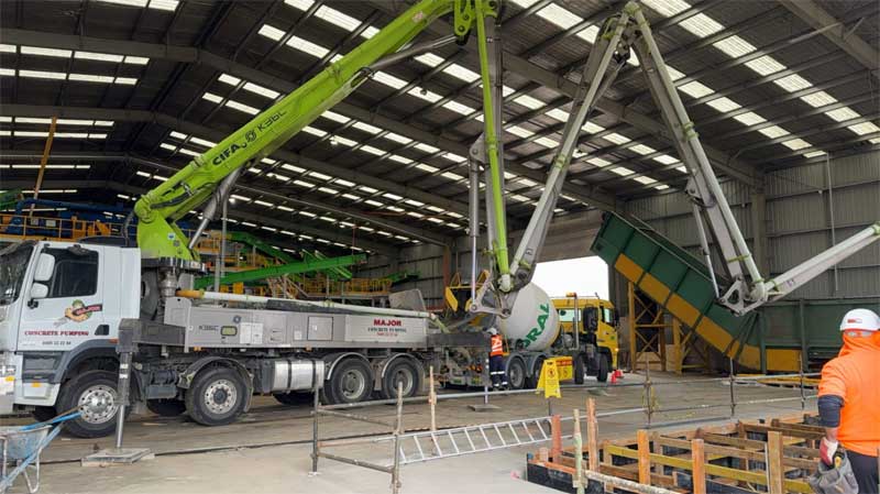 Concrete pump truck and agitator pouring inside a large open shed