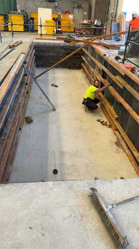 Worker in hi-vis setting up timber formwork for a concrete pit inside a factory