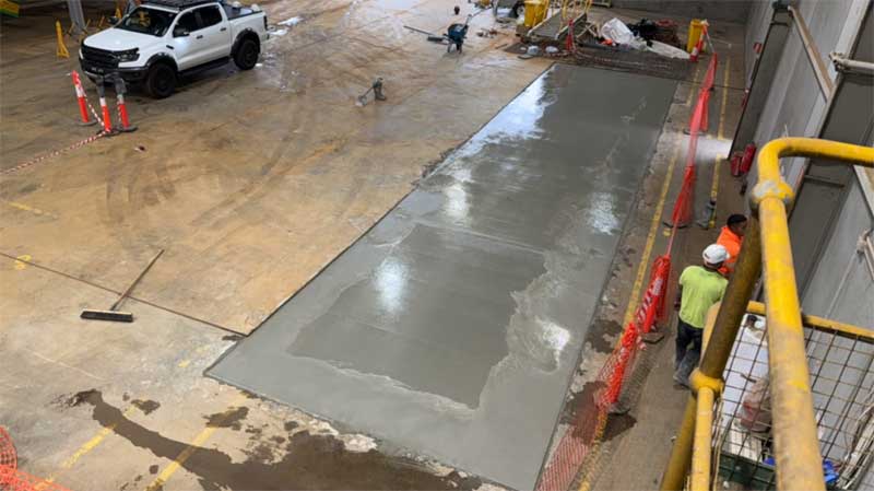 Fresh concrete strip poured into a factory floor beside a ute and safety railing