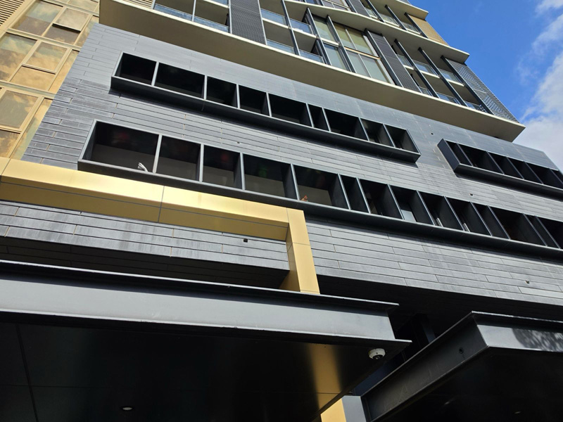 Looking up at a multi-storey apartment building with dark cladding and gold trim