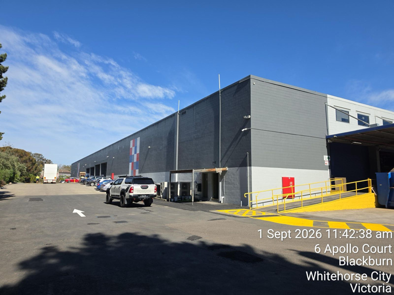 Large grey warehouse with a car park and a yellow-marked loading ramp