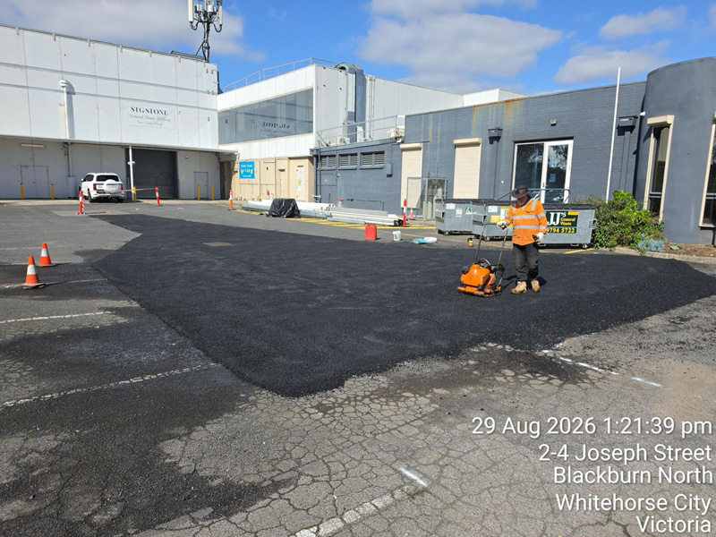 Worker compacting a fresh asphalt patch in a car park with a plate compactor