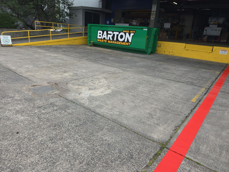 Concrete loading area with a red painted line and a green skip bin