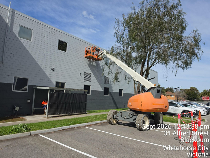 Boom lift working on the upper wall of a grey commercial building